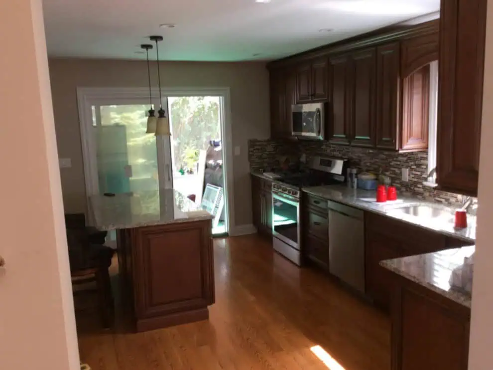 Modern kitchen with wooden cabinets, stainless steel appliances, granite countertops, and a hardwood floor by MHI Renovation Services Inc., viewed from an adjacent room.