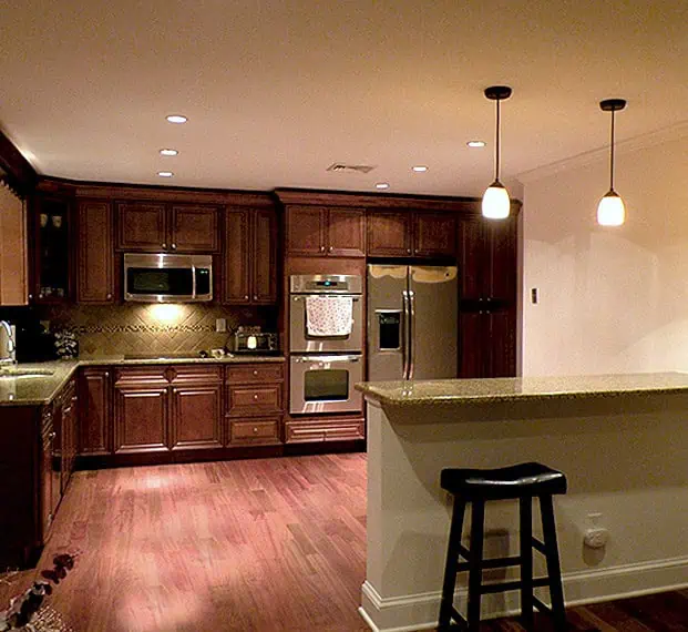 Modern kitchen with dark wood cabinets, stainless steel appliances, hardwood floors, and pendant lights over a bar with stools renovated by MHI Renovation Services Inc.