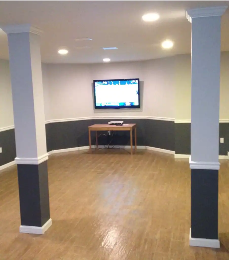 A basement living area with green walls featuring two white columns, hardwood flooring, and a television on a small wooden st