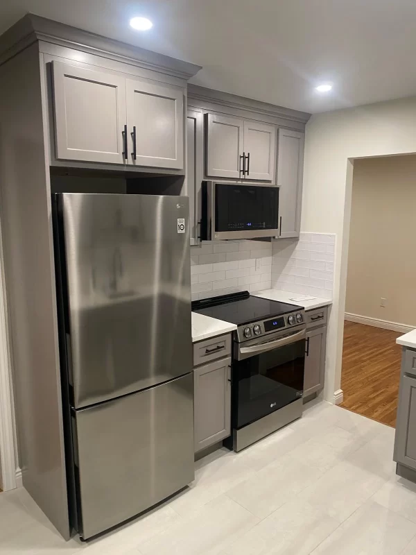 A modern kitchen with stainless steel appliances, gray cabinets, white subway tile backsplash, and home remodeling services.